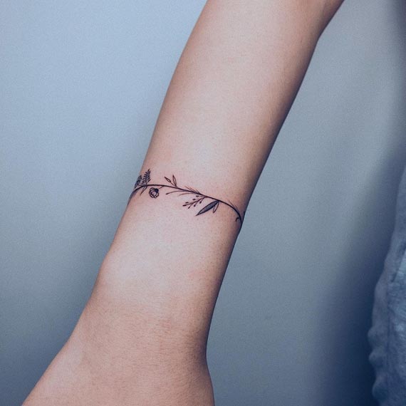 floral tiny flowers wildflower branch leaves and stems armband tattoo minimalist female lower forearm 1