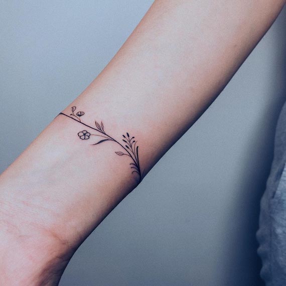 floral tiny flowers wildflower branch leaves and stems armband tattoo minimalist female lower forearm 2