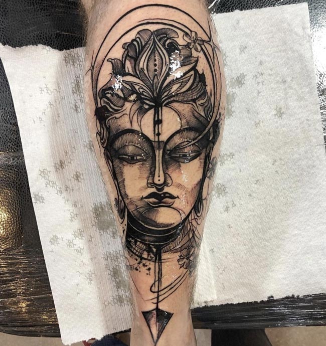 inverted crescent moon and lotus flower on head of buddha face below arrow tattoo male calf