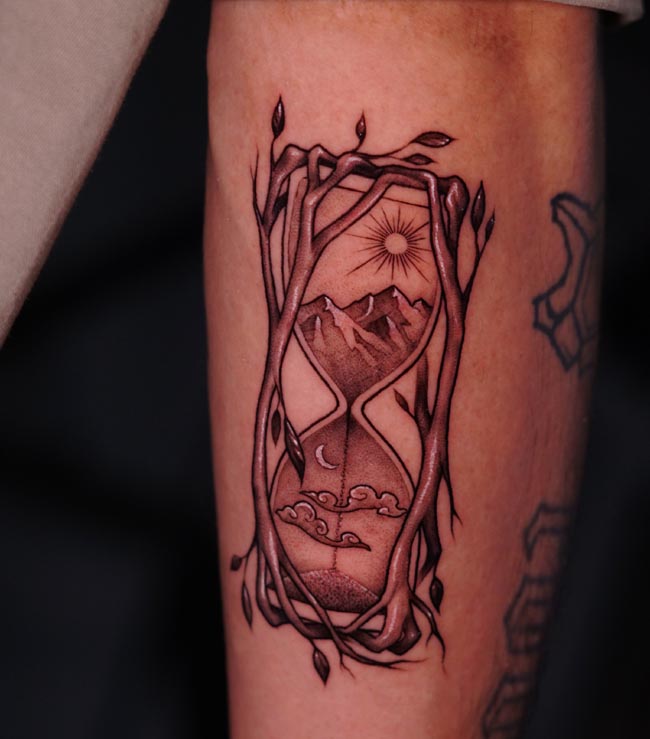 hourglass-mountains-sun-moon-clouds-landscape-tree-branches-vines-leaves-tattoo-male-arm