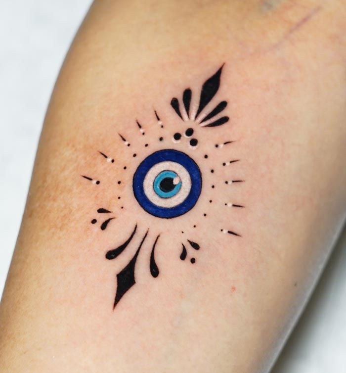 evil eye colored tattoo with ornamental touch female arm