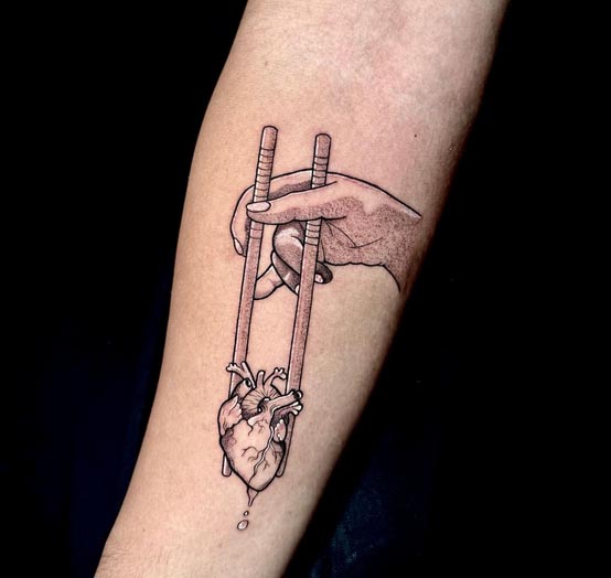hand holding heart with chopsticks tattoo woman forearm