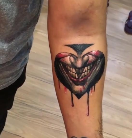 heart shaped joker face tattoo design male hand forearm