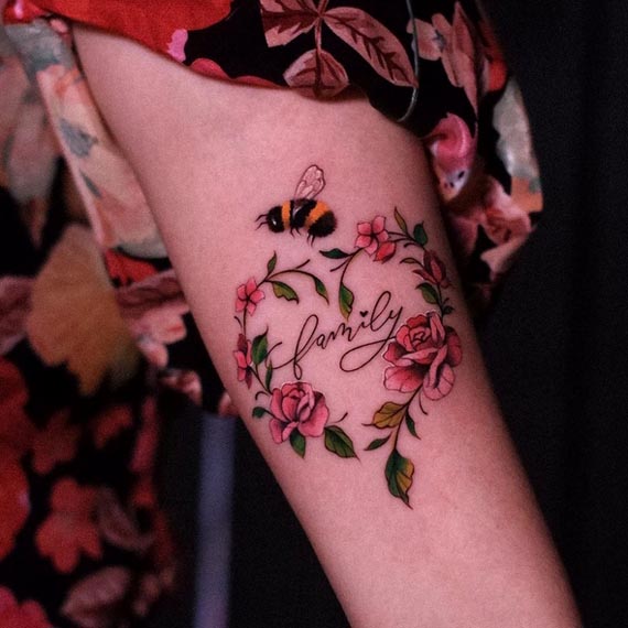 roses and leaves in heart shape with bee and word family tattoo design female hand forearm