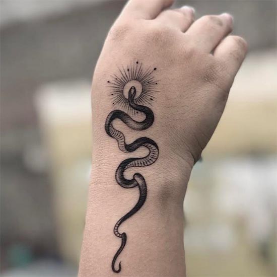 minimalist snake with sun tattoo design female hand wrist