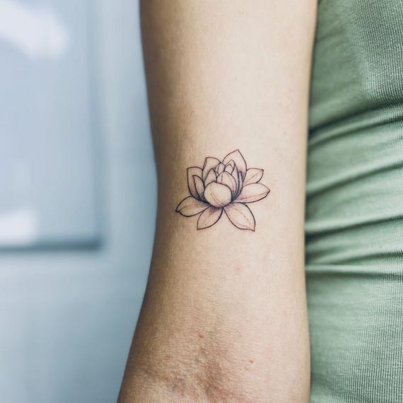 small lotus fineline tattoo design female bicep
