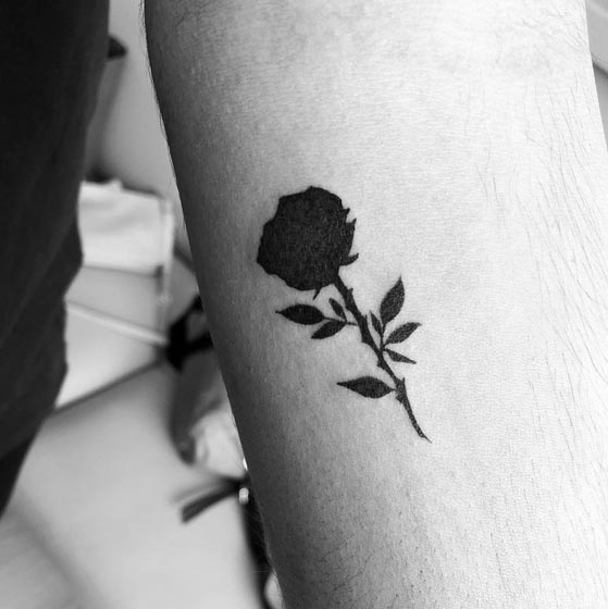 silhouette small rose with stem leaves tattoo female hand forearm