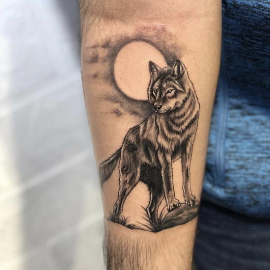 standing wolf and moon in background tattoo design male forearm